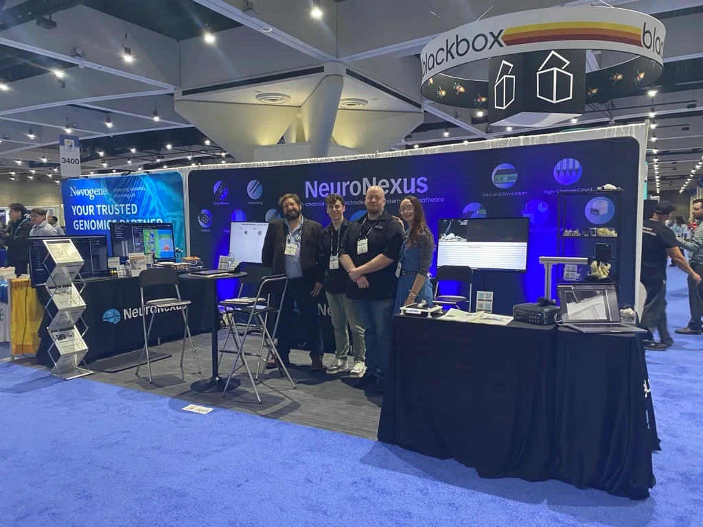 The NeuroNexus booth at Neuroscience 2025: four members of the team standing in front of the NeuroNexus backdrop, with recording systems, monitors and probe displays on the tables